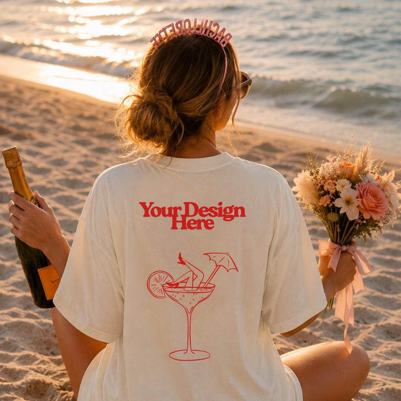 May include: An off-white t-shirt featuring red text that reads Your Design Here above a red line art graphic of a cocktail glass containing legs with high heels, a citrus slice, and a small umbrella, worn with a pink Bachelorette headband.