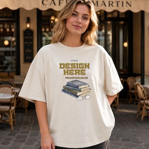 May include: An off-white short-sleeve t-shirt featuring the text "YOUR DESIGN HERE" in a bold, olive-green font, followed by "PRIMEPIXELMUSE" in smaller letters, and a graphic illustration of a stack of three books with a pair of wire-rimmed glasses.