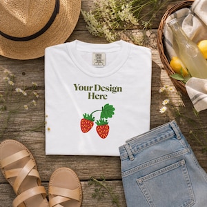 Może przedstawiać: Biały t-shirt z krótkim rękawem z napisem Your Design Here ciemnozielonymi literami nad grafiką przedstawiającą dwie czerwone truskawki z zielonymi liśćmi. Koszulka posiada metkę marki Comfort Colors przy kołnierzu z rozmiarem L G G.