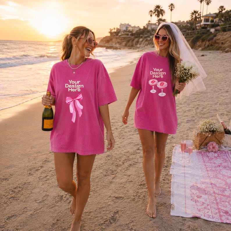 May include: Two bright pink oversized t-shirts featuring white text that reads Your Design Here. One shirt displays a pink ribbon graphic, while the other shows a graphic of two cocktail glasses. Both shirts have short sleeves and a crew neckline.