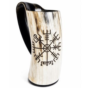 May include: A drinking horn made from natural material with a polished cream and brown marbled surface. The exterior features a dark, laser-engraved Vegvisir symbol. The interior and the curved handle are a solid, deep black colour.