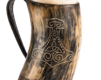 May include: A curved drinking horn mug with a dark brown and tan mottled finish, featuring a carved Mjolnir hammer symbol on the front. The mug has a dark handle and a flat wooden base, filled to the brim with a thick, light-colored foam head.