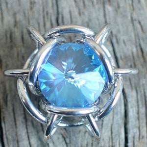 May include: A silver wire cage with a light blue crystal in the centre.