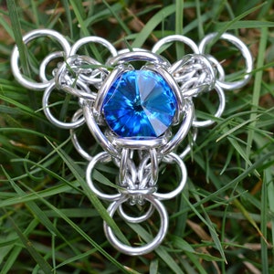 May include: A silver chainmail pendant featuring a large, faceted, blue gemstone at its centre.