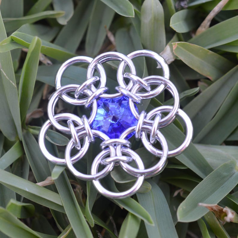 May include: A silver chainmail flower with a blue gemstone in the center.