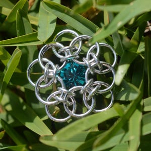 May include: A silver chainmail flower with a teal gemstone in the center.