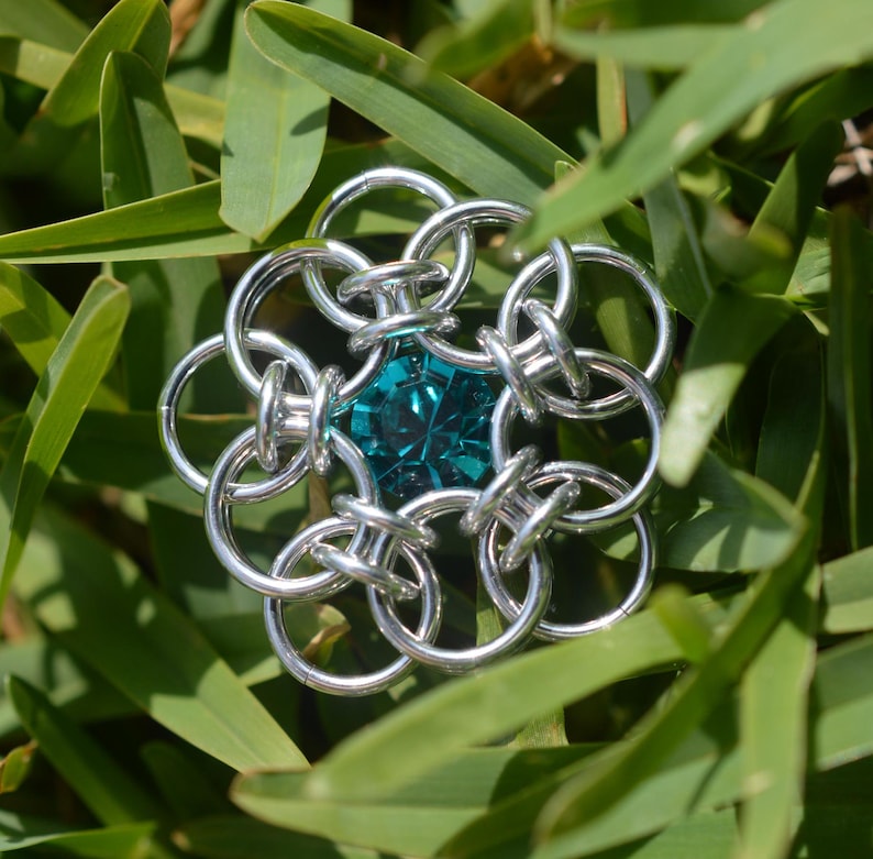 May include: A silver chainmail flower with a teal gemstone in the center.