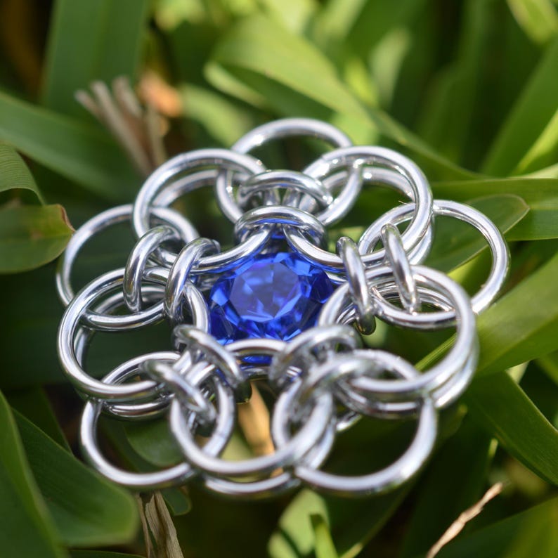 May include: A silver chainmail flower with a blue gemstone in the center.