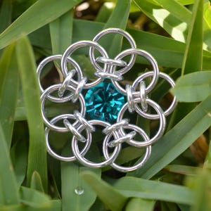 May include: A silver metal chainmail flower with a teal blue gemstone in the center.