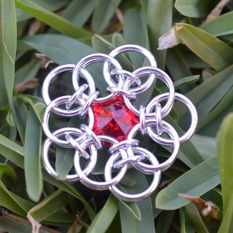 May include: A silver chainmail flower with a red gemstone in the center.