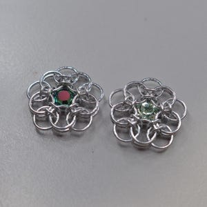 May include: Two silver chainmaille flower charms with a green and red gemstone in the center of each.