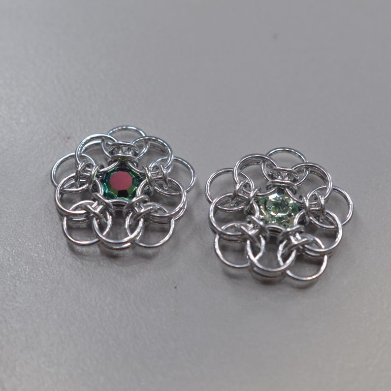May include: Two silver chainmaille flower charms with a green and red gemstone in the center of each.