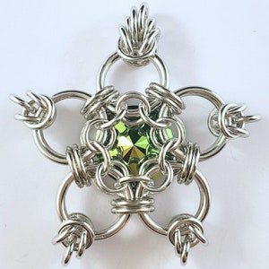 May include: A silver metal snowflake pendant with a green gemstone in the centre. The snowflake is made of interlocking rings.
