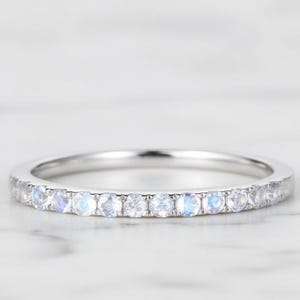 May include: A silver band ring set with small, round, light blue gemstones. The gemstones are evenly spaced around the ring. The ring is displayed on a white marble surface.