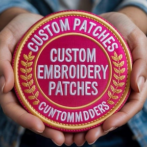 May include: A circular embroidered patch with a vibrant pink background and a gold border. The text reads CUSTOM PATCHES, CUSTOM EMBROIDERY PATCHES, and CUNTOMMDDERS in white, with two gold laurel leaf branches flanking the central text.