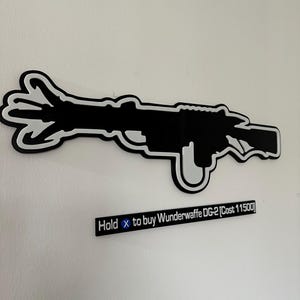 May include: Black and white wall art of a stylized gun. The art piece has a white outline and a black interior. Below the gun is a black rectangle with the text "Hold x to buy Wunderwaffe DG-2 [Cost 11500]"