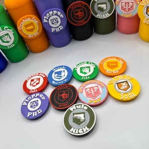 May include: A selection of brightly coloured bottle-shaped items and circular coasters. The bottles are in shades of green, orange, purple, black, and pink. The coasters display distinctive designs and text, including "Double Tap," "Widow's Wine," and "Mule Kick."