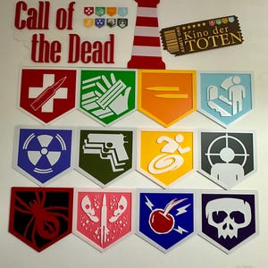 Pode incluir: Uma coleção de decorações de parede coloridas e estilizadas com vários símbolos e ícones. As decorações incluem um farol vermelho, um bilhete que diz "Kino der Toten" e vários emblemas em forma de escudo com designs e cores únicos. As palavras "Call of the Dead" também estão presentes.