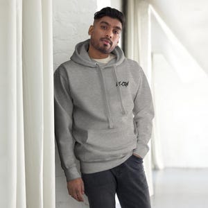 May include: A heather gray hoodie with a front pocket and a drawstring hood. The hoodie features the text "X-CON" in black on the upper chest. The person in the image is wearing the hoodie.