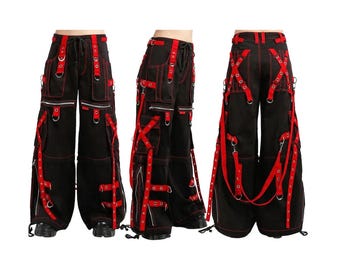 May include: Black cargo pants with red accents, featuring multiple pockets, zippers, and straps. The pants have a wide leg design and are displayed from multiple angles, showcasing the details of the construction.