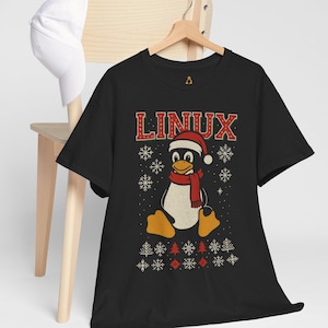 May include: Black t-shirt with a festive design featuring a penguin in a Santa hat and scarf, and the word "LINUX". The design includes snowflakes and Christmas tree patterns, creating a holiday theme.
