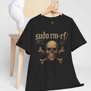 May include: Black t-shirt featuring a skull and crossbones graphic with the text "sudo rm -rf/". The design is in shades of brown and gold. A white baseball cap hangs on a wooden chair in the background.