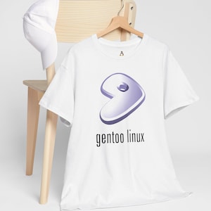 Peut inclure: T-shirt blanc avec le logo Gentoo Linux, un design violet et blanc stylisé, et le texte "gentoo linux" en noir. Une casquette de baseball blanche est posée sur une chaise en bois.
