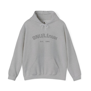 May include: A light gray hoodie with a front pocket and drawstring hood. The text "GNU/Linux Est. 1991" is printed in black on the front. The hoodie is made of a soft, comfortable material.