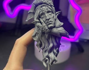 May include: A grey, detailed bust of a fantasy character with long, flowing hair, pointed ears, and armour. The figure rests their chin on their hand, with a contemplative expression. The bust is mounted on a small, textured base.