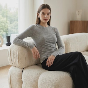 Puede incluir: Una camiseta de manga larga gris con cuello redondo combinada con pantalones negros. La camiseta presenta una silueta ajustada con un escote redondo sencillo y mangas largas, mientras que los pantalones son de color negro liso y corte recto.