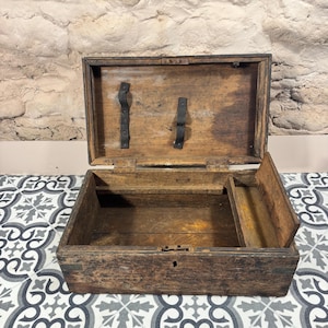 May include: An open, antique wooden chest with a hinged lid and a small interior compartment. The chest is made of dark, weathered wood with visible grain and metal accents. The interior is empty, revealing the chest's construction and age.