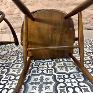 May include: A vintage wooden chair, viewed from below, showcasing its dark brown, aged wood construction. The chair has a rounded seat and four angled legs. The image highlights the chair's joinery and the wear and tear of time.