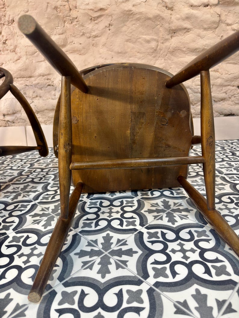 May include: A vintage wooden chair, viewed from below, showcasing its dark brown, aged wood construction. The chair has a rounded seat and four angled legs. The image highlights the chair's joinery and the wear and tear of time.