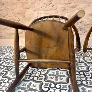 May include: A vintage wooden chair with a curved back and spindle detailing. The chair has a natural wood finish and a sturdy, traditional design. The legs are angled for stability, and the seat appears to be made of solid wood.