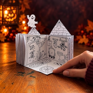 Może przedstawiać: Miniaturowa papierowa książka typu pop-up z czarno-białymi ilustracjami liniowymi wnętrza nawiedzonego domu. Strony przedstawiają ducha, pajęczyny, lustro i butelki z miksturami. Konstrukcja wykonana jest z białego papieru ze szczegółowymi rysunkami.