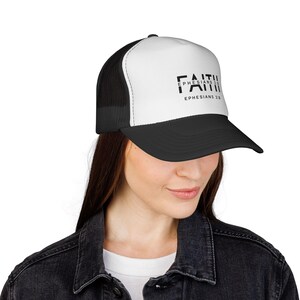 May include: A black and white trucker hat with the word "FAITH" printed in black, along with "EPHESIANS 1:1" and "EPHESIANS 2:8". The hat has a white front panel, a black brim, and a black mesh back.