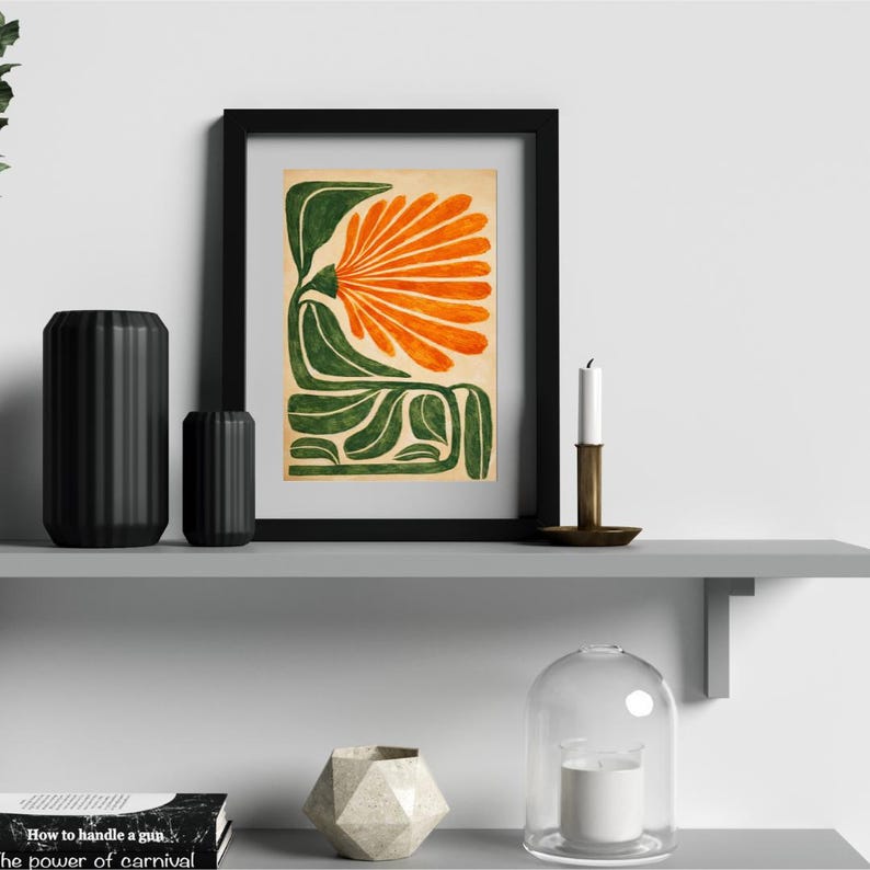 May include: A framed art print featuring an abstract floral design in orange and green. The artwork is displayed on a gray shelf with black decorative vases, a candle, and other decor. The print is in a black frame.