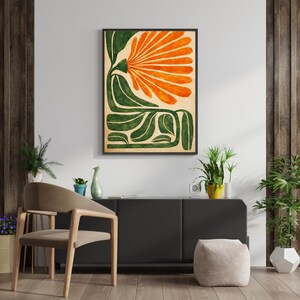 May include: Abstract art print featuring a stylized orange flower with green leaves against a beige background. The artwork is framed in a black border and hangs on a white wall. The print adds a touch of nature-inspired decor.