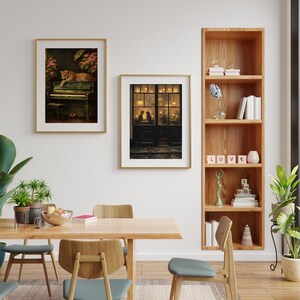 May include: Two framed art prints hang on a white wall. One features a leopard on a piano, the other depicts a couple in a doorway. A wooden bookshelf displays books and decorative items. A wooden dining table and chairs are in the foreground.