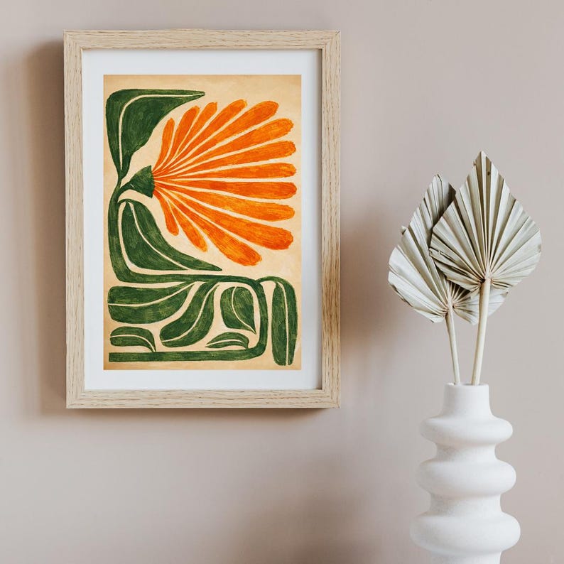 May include: Abstract art print in a light wood frame. The artwork features a stylized orange flower with green leaves and stems on a beige background. A white vase with dried palm leaves is in the foreground.