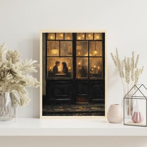 May include: A framed print depicts a romantic scene of a couple dining in a warmly lit restaurant. The artwork features a dark wooden door with glass windows, through which the couple is visible, illuminated by candlelight. The overall color palette is warm and inviting.
