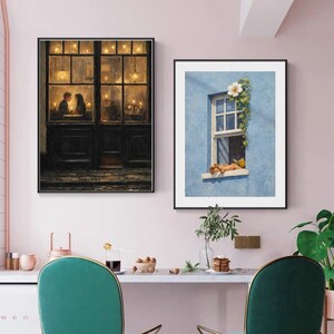 May include: Two framed art prints. One depicts a couple dining in a warmly lit restaurant. The other shows a person relaxing in a window with a white flower and green vines against a blue wall. The prints are displayed above a table with green chairs.