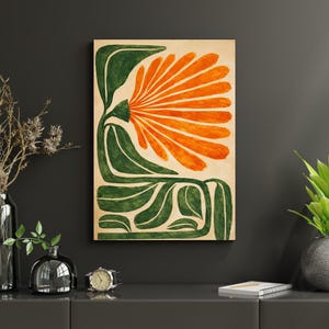 May include: Abstract floral art print featuring a large orange flower with green leaves and stems against a beige background. The artwork is mounted on a wooden panel and displayed on a dark gray wall. The style is reminiscent of mid-century modern art.