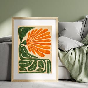May include: A framed art print featuring a stylized orange flower with green leaves and stem. The artwork is set against a beige background and framed in a light wood frame. The floral design is a bold, modern interpretation.