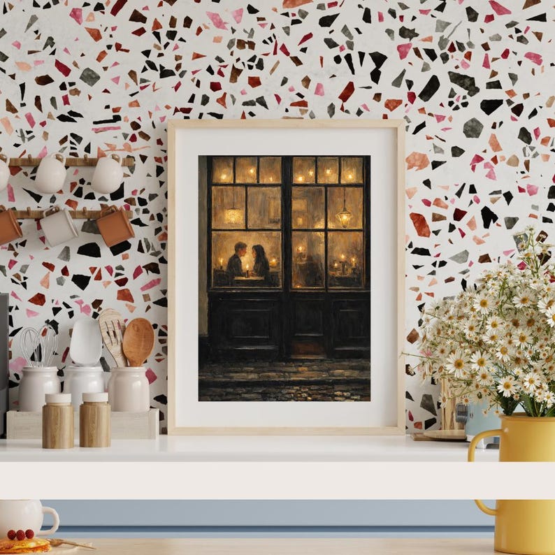 May include: A framed print depicts a romantic scene of a couple dining in a warmly lit restaurant. The artwork features a dark wooden door and window frame, with soft lighting and a cozy atmosphere. The background has a colorful terrazzo pattern.