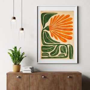 May include: A framed art print featuring a stylized floral design. The artwork showcases a large orange flower with green leaves and stems against a beige background. The print is displayed in a white frame, adding a modern touch to the botanical theme.
