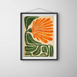 May include: Framed art print featuring a stylized floral design. The artwork showcases a large orange flower with radiating petals, set against a beige background. The flower is supported by green, curved leaves and stems. The print is encased in a black frame.