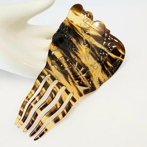 May include: A brown and black tortoiseshell hair comb with a decorative, openwork design. The comb has five teeth.
