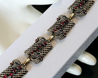 May include: Gold tone bracelet with a woven design and red rhinestone accents.