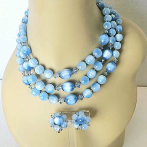 May include: A three-strand light blue glass bead necklace with clear crystal accents and matching light blue glass bead earrings.